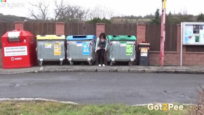 A bit plump amateur brunette gal squats down and pisses between refuse bins