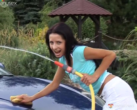 Slender brunette is washing a car and playing with hose