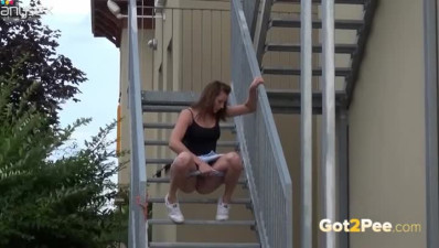 Filthy dark haired chick sits on stairs outdoors and pisses