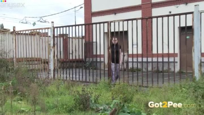 Dark haired attractive chick pisses on metal fence