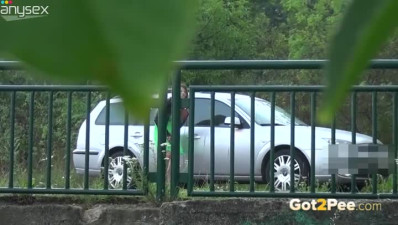 Dark haired filthy woman in green dress makes metal fence wet with her pisses